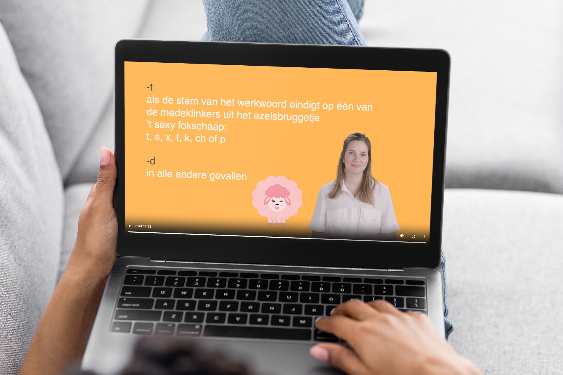 Op de schoot van een persoon staat een laptop met een schermafbeelding van een video uit de Van Dale E-learning Werkwoordspelling