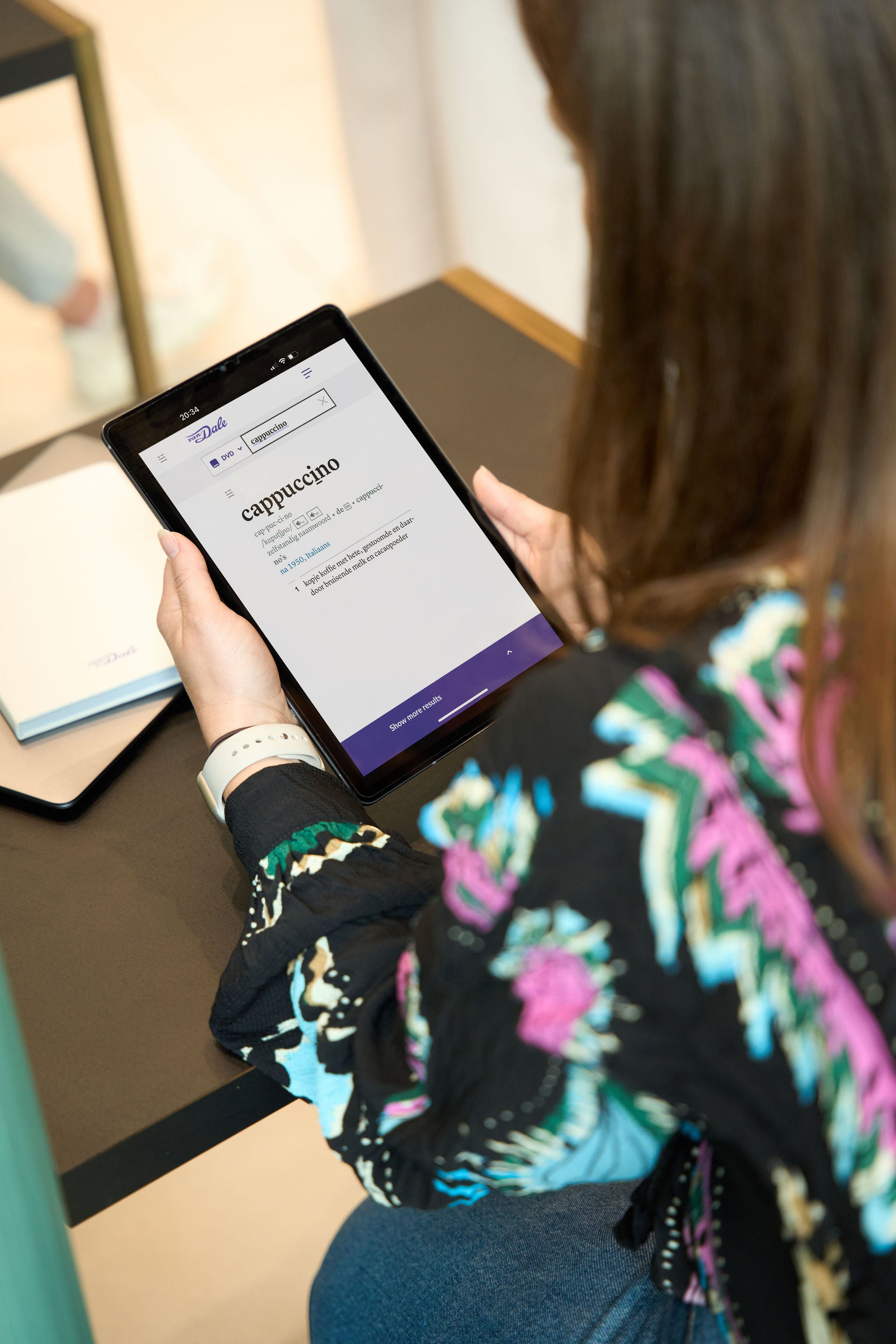 Een student is over een tablet gebogen met een schermafbeelding van Van Dale Online met de definitie van het woord 'cappuccino'